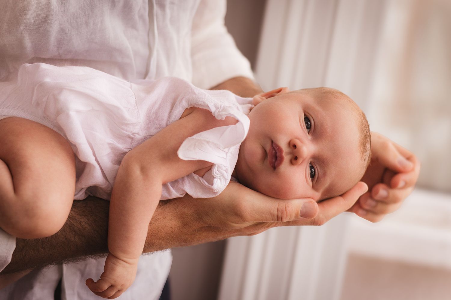 Baby wearing white outfit lying on soft white bedding.