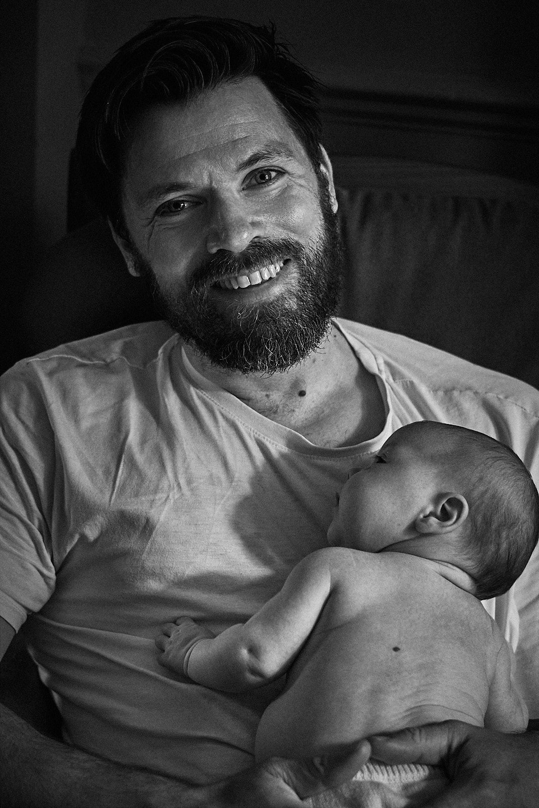 A black and white portrait of a parent holding a sleeping newborn baby.
