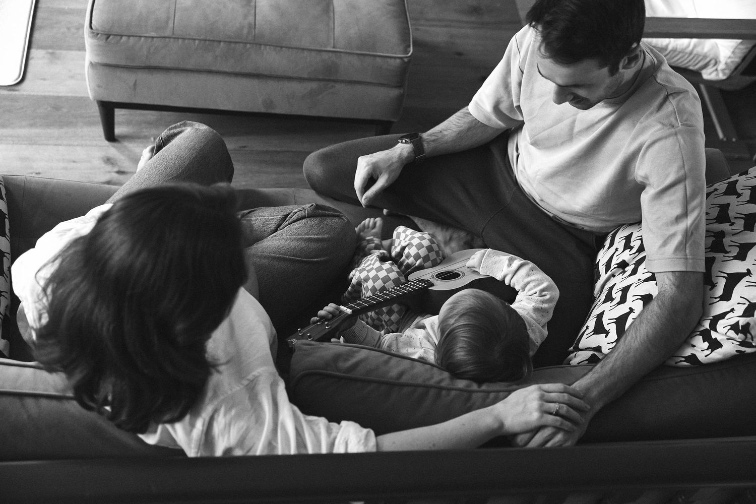 Black and white photo of parents and baby relaxing together on couch in intimate family moment.