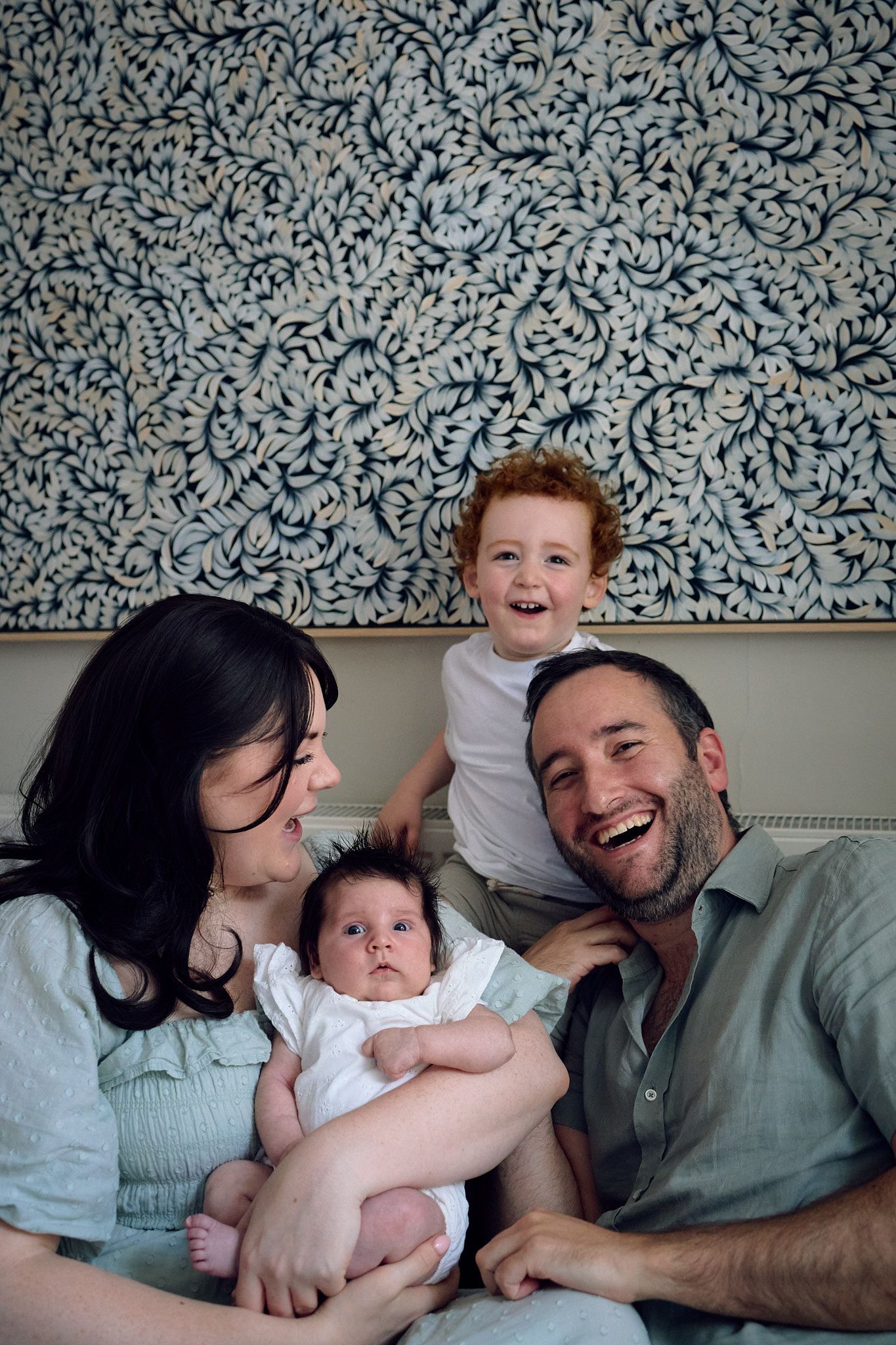 A happy family portrait against a decorative blue and white patterned wall.