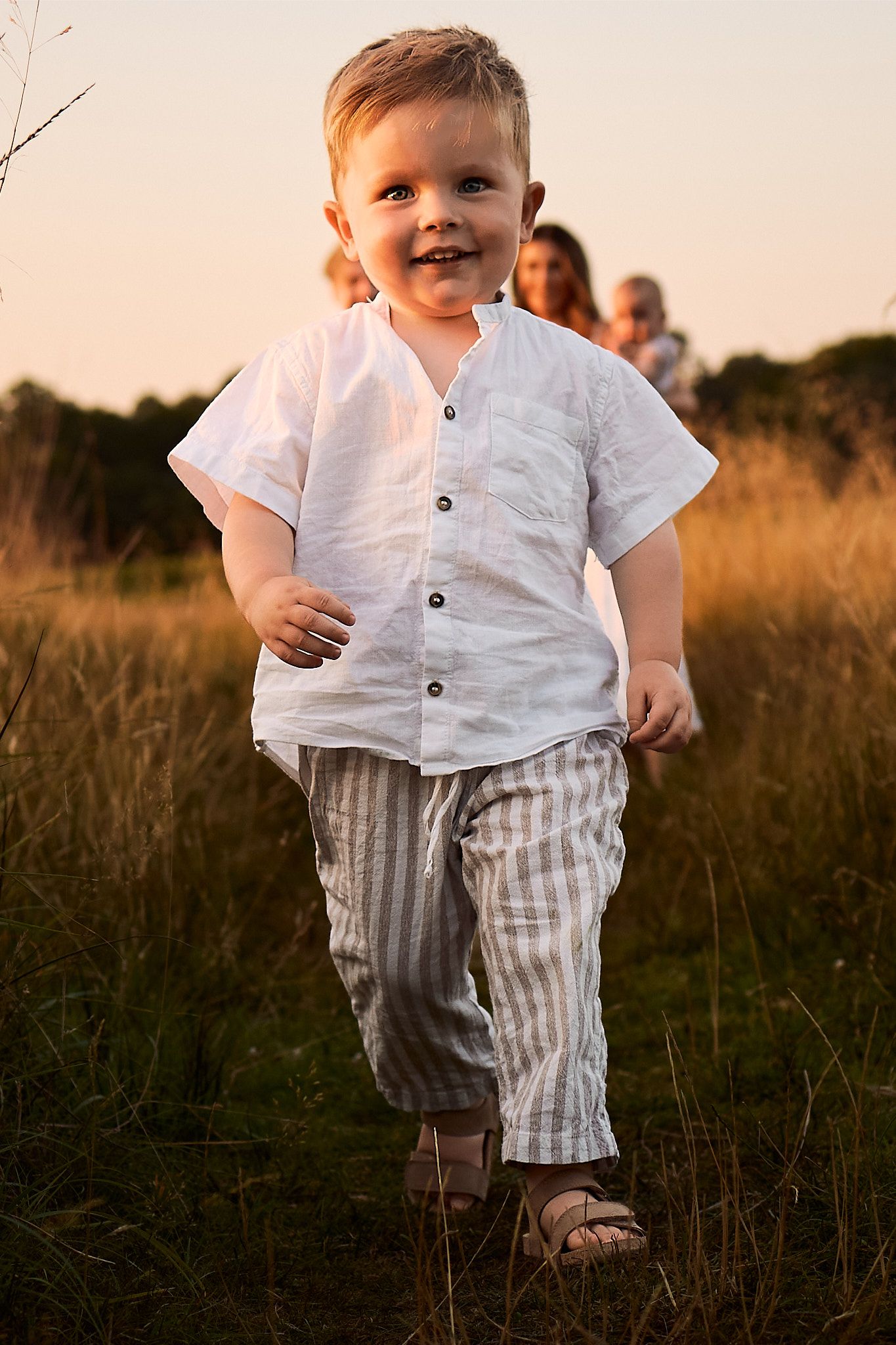 Young child in white shirt and striped shorts walking through golden field at sunset.