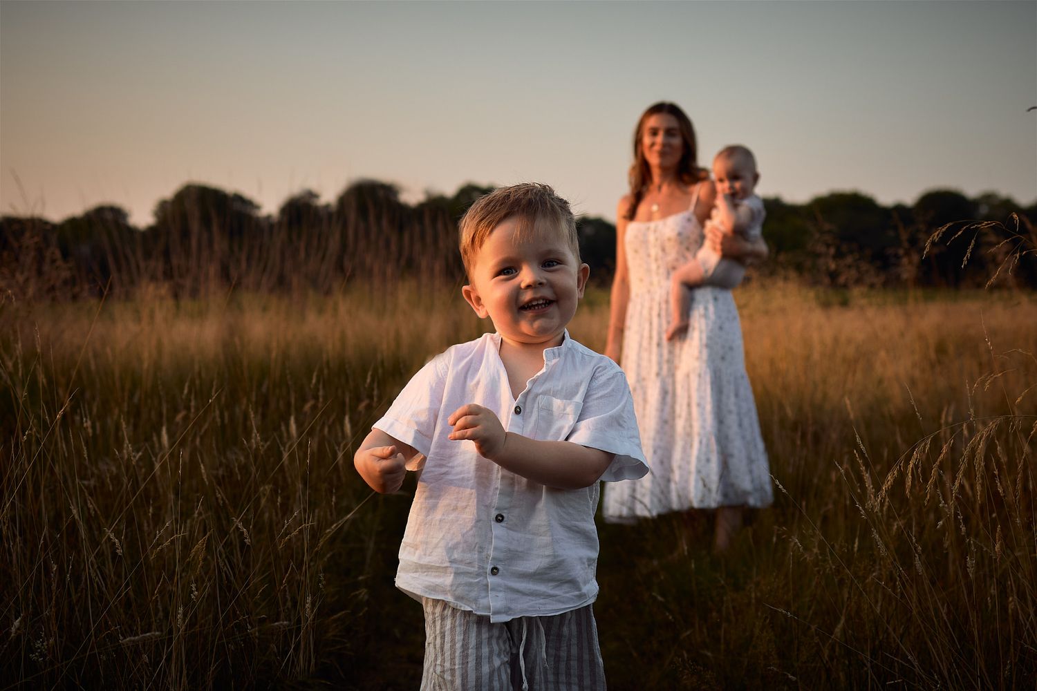 A child laughs joyfully in a field while family stands in background during golden hour.