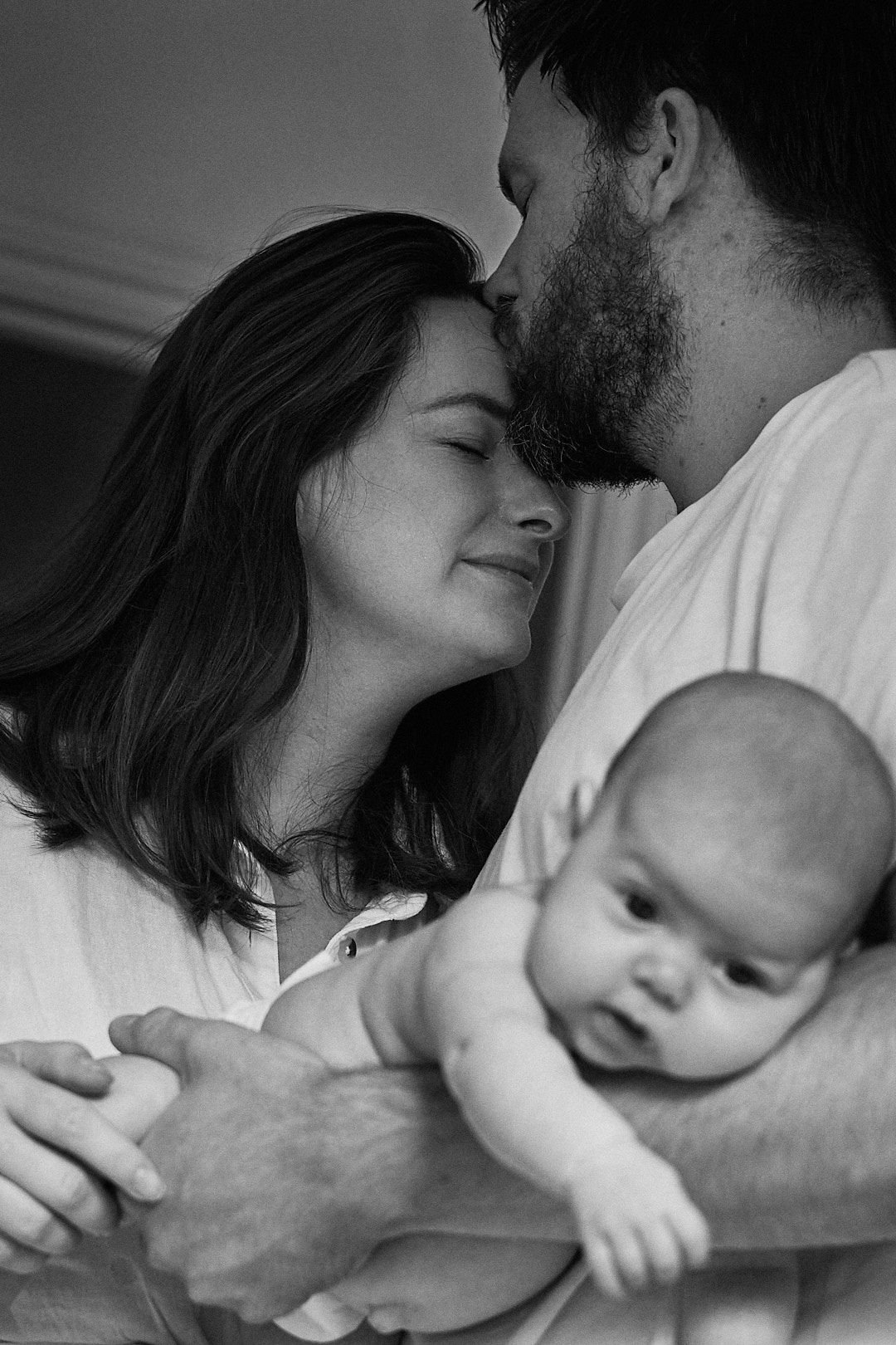 An intimate black and white family portrait showing tender moments with a young infant.