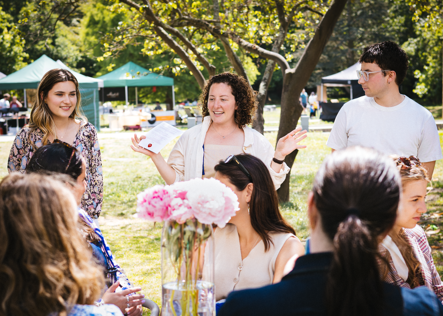 People enjoying conversation at an outdoor social gathering with pink floral decorations.