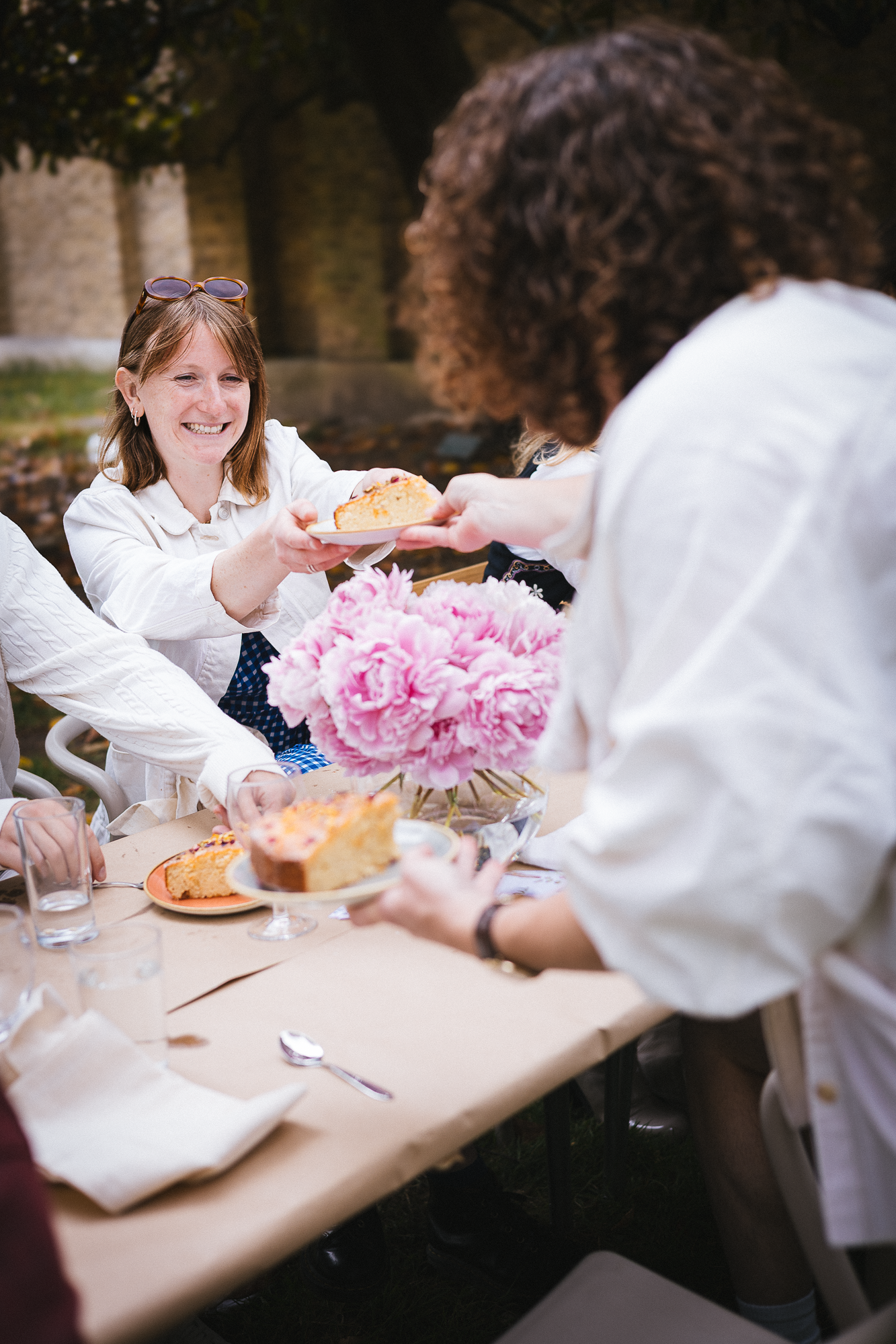 Group enjoys casual dining at outdoor table decorated with pink floral centerpiece.