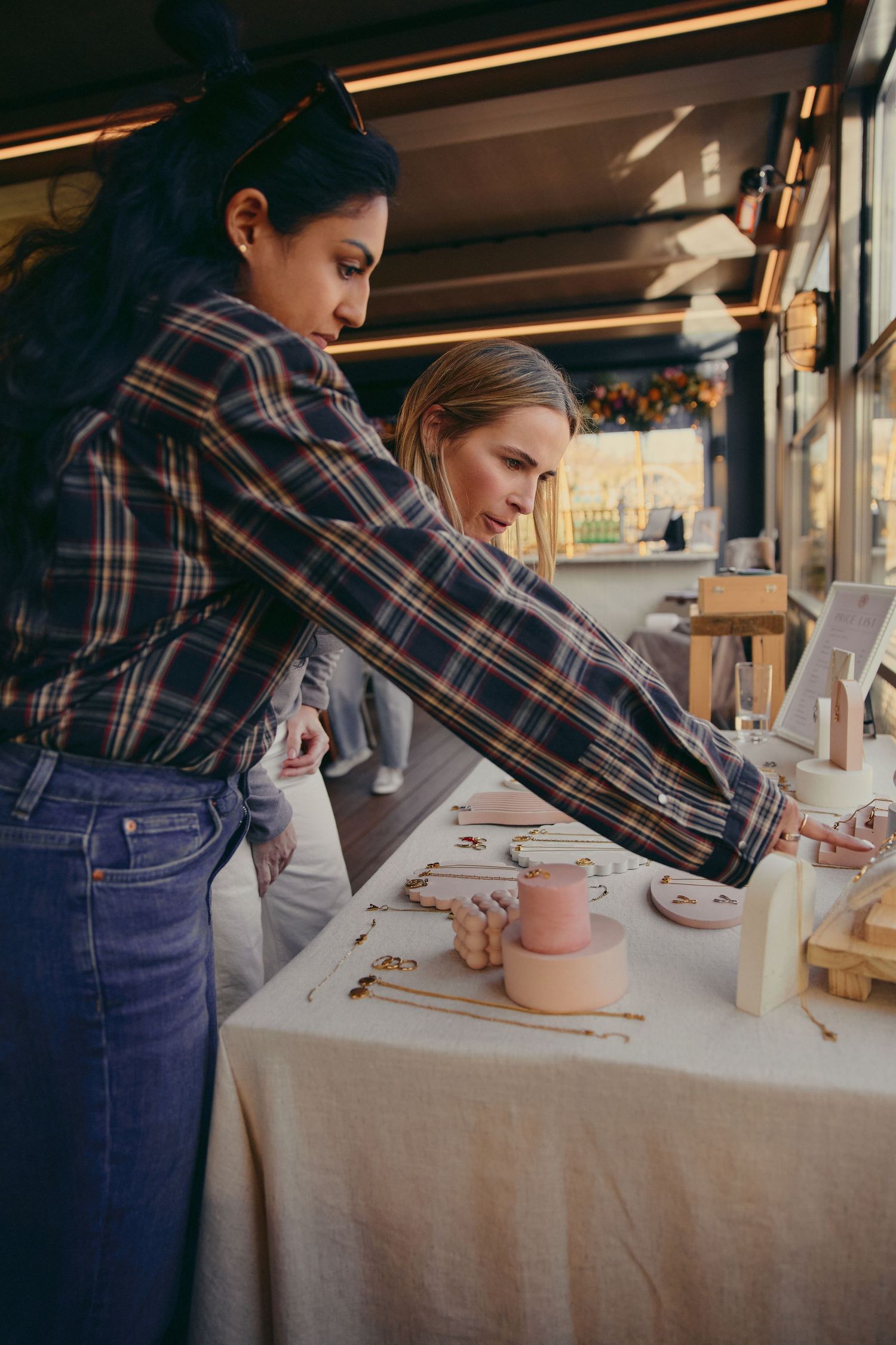 Two women examine handmade ceramic pottery displayed on a table in a craft studio.