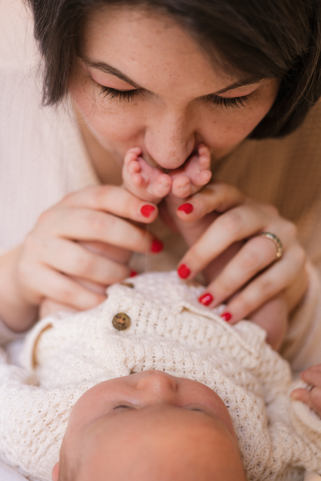 Gentle nurturing moment captured as hands with red nails cradle a peaceful sleeping baby.