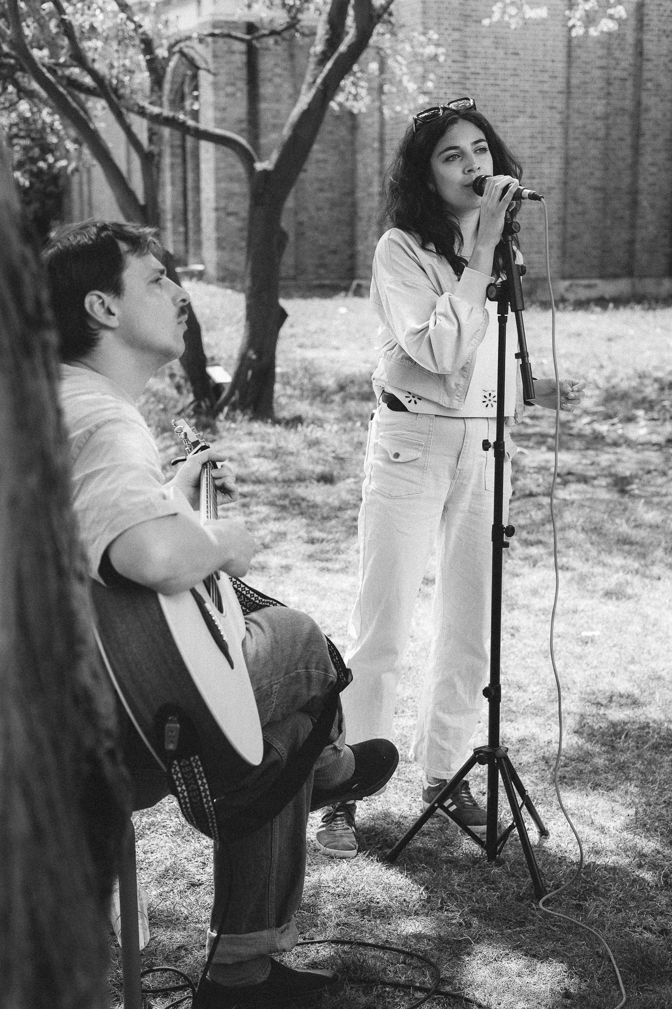 Musicians performing outdoors near brick buildings with instruments and microphone stands.