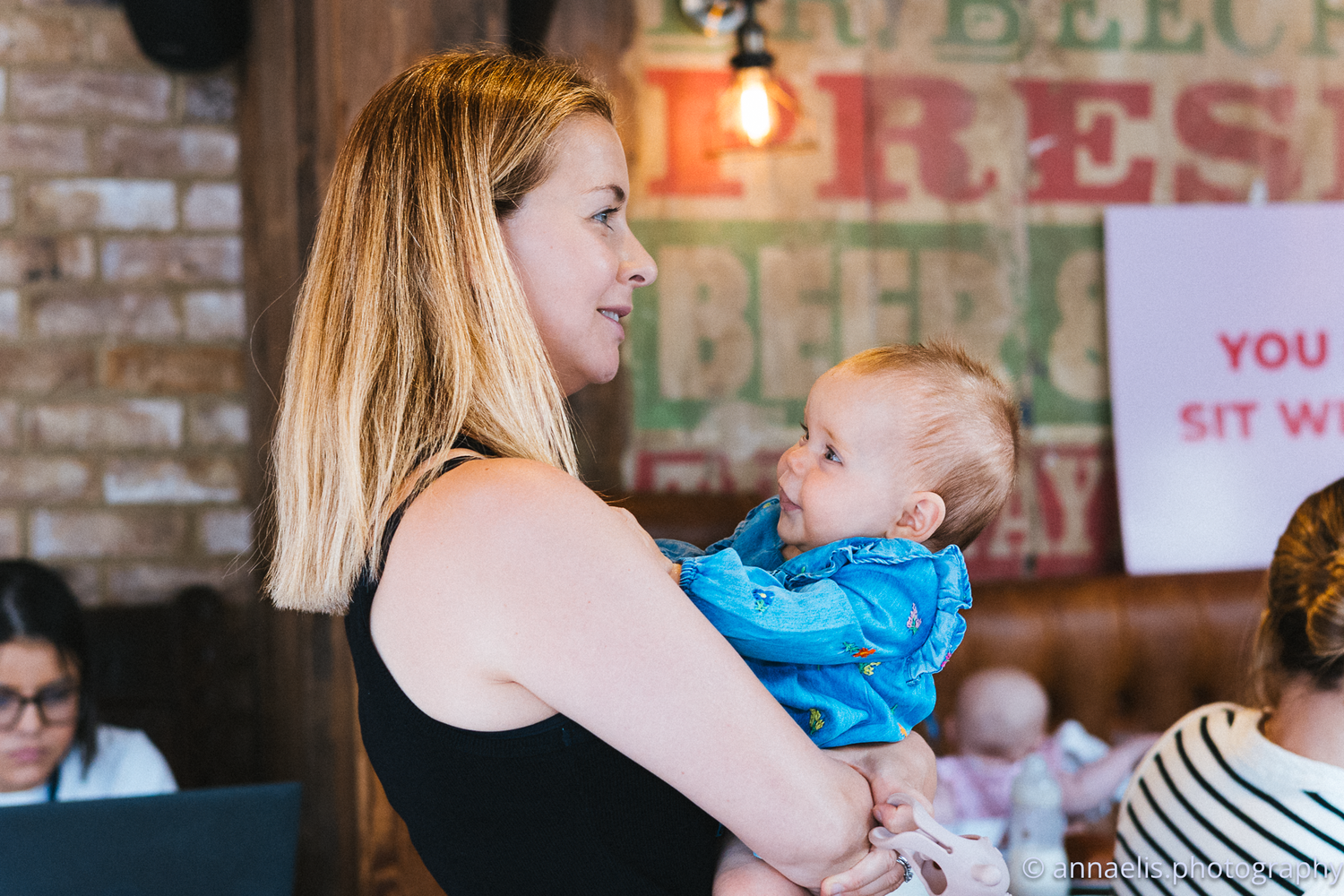 Parents and infants gather in a casual restaurant setting with brick walls.
