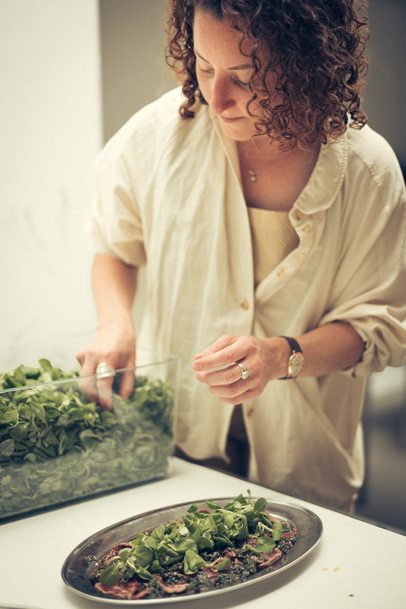 Chef in white shirt carefully adding fresh greens to prepared dish.