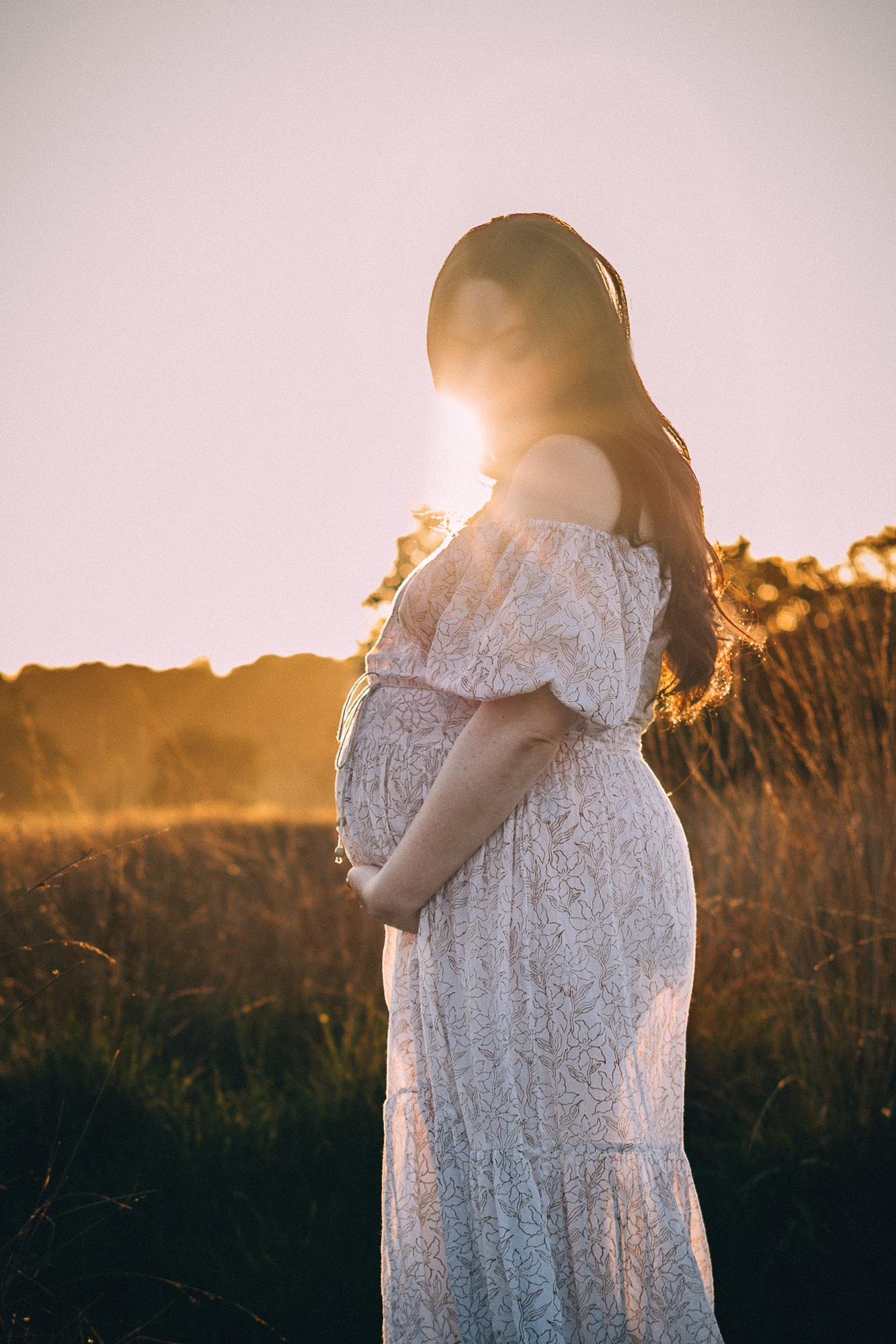 Silhouette of woman in white dress against warm sunset glow.