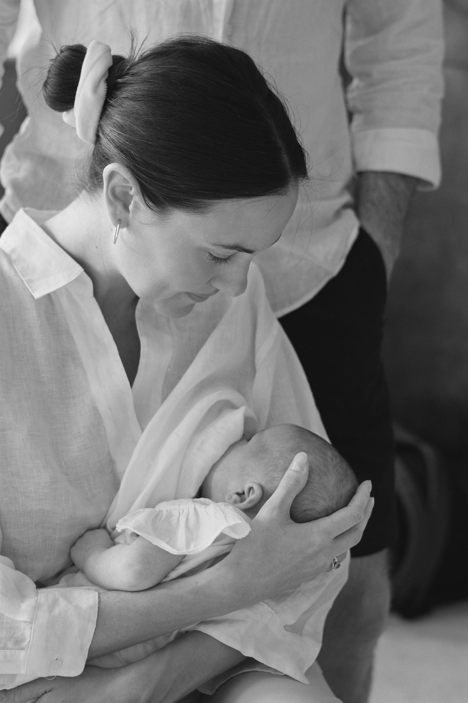 Black and white photo of a mother tenderly cradling her newborn baby, wearing a white shirt.