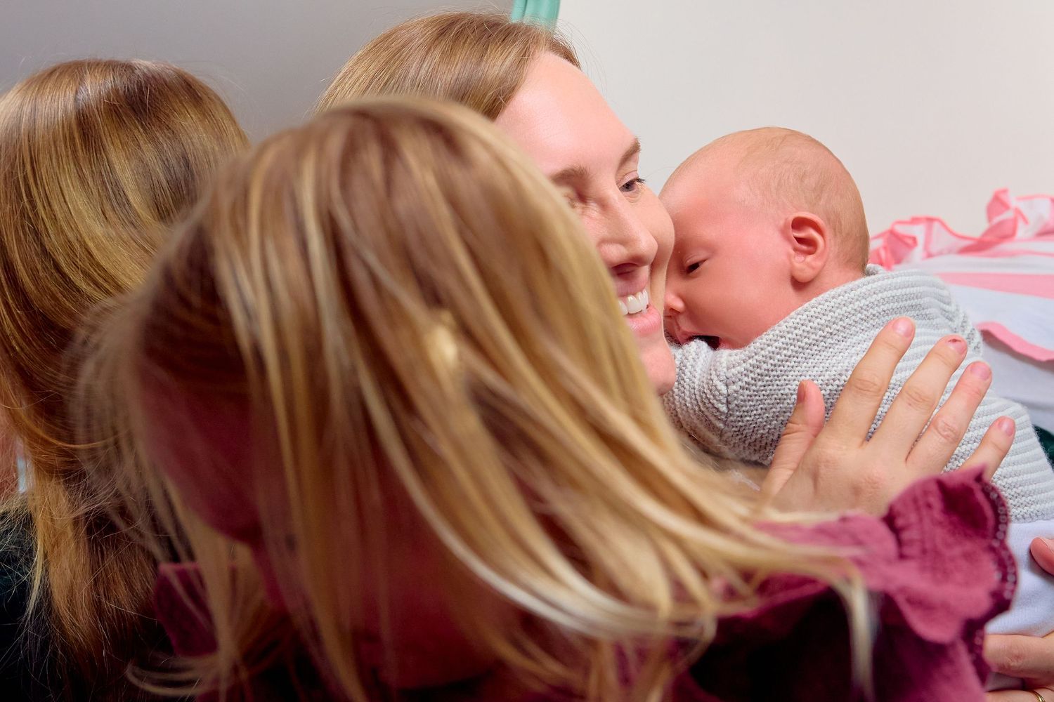 Woman smiling and nuzzling a newborn baby while another woman with blonde hair looks on closely.