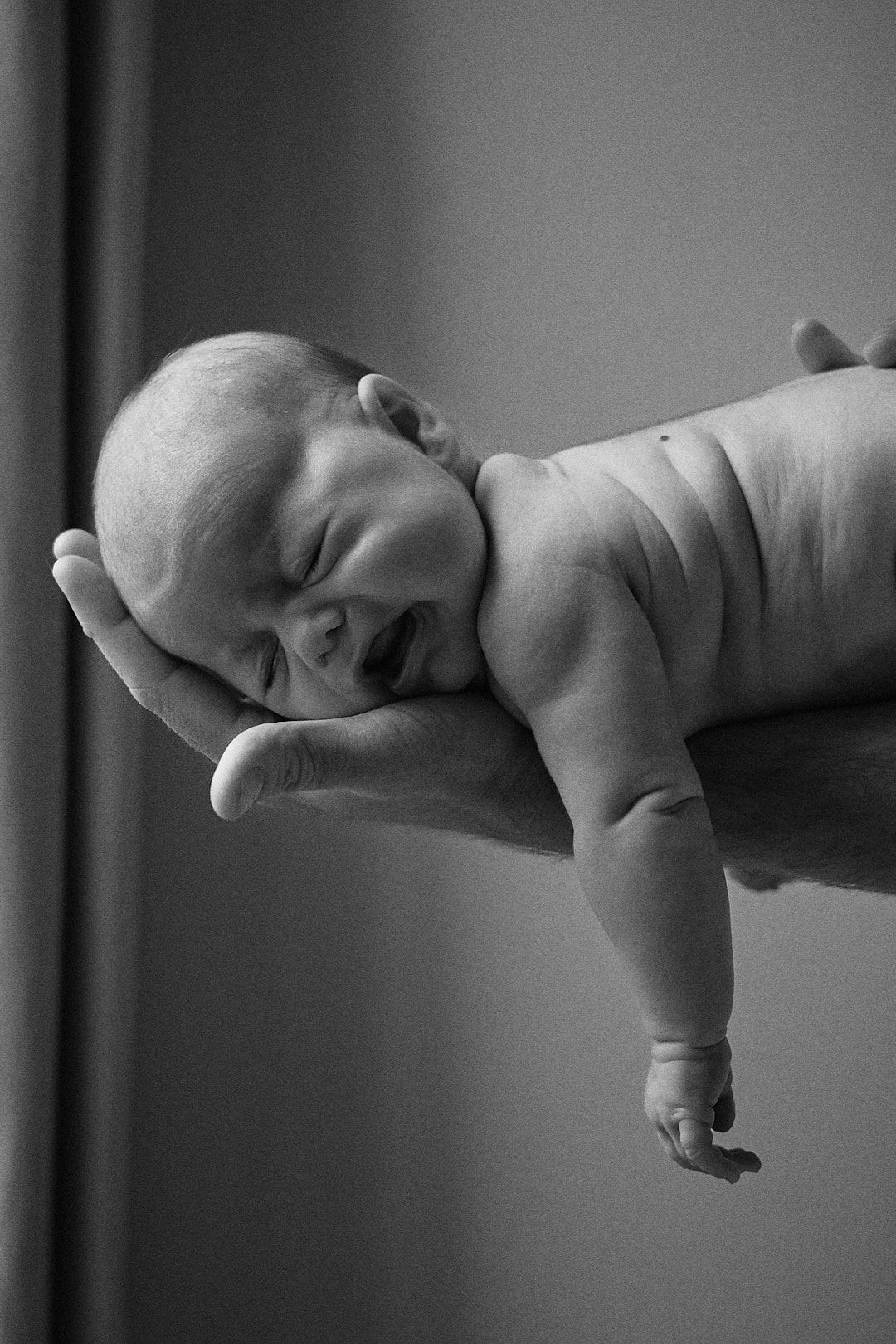 Black and white profile of sleeping newborn stretched out against neutral background.