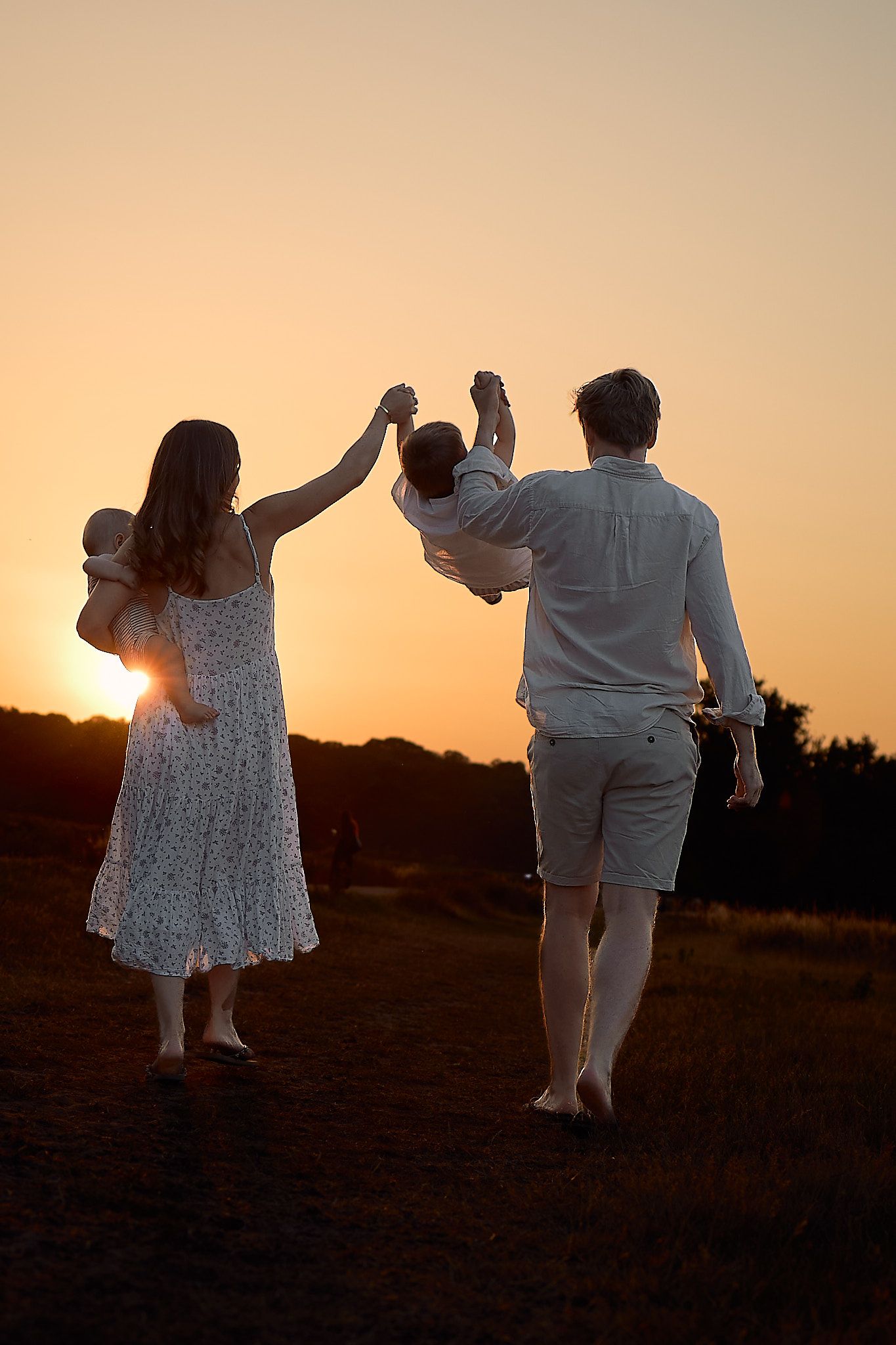A family lifts their child in the air against a sunset backdrop.