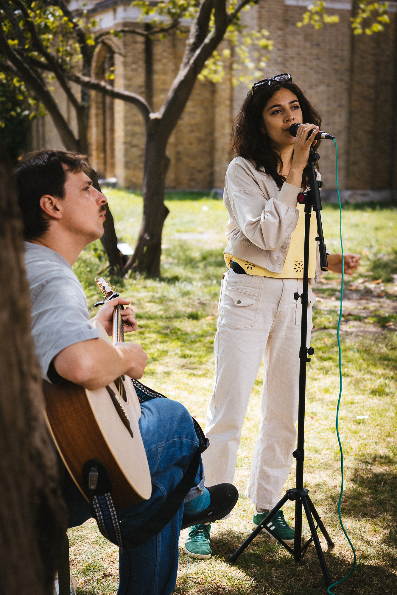Musicians perform in a shaded outdoor setting with microphone stands.