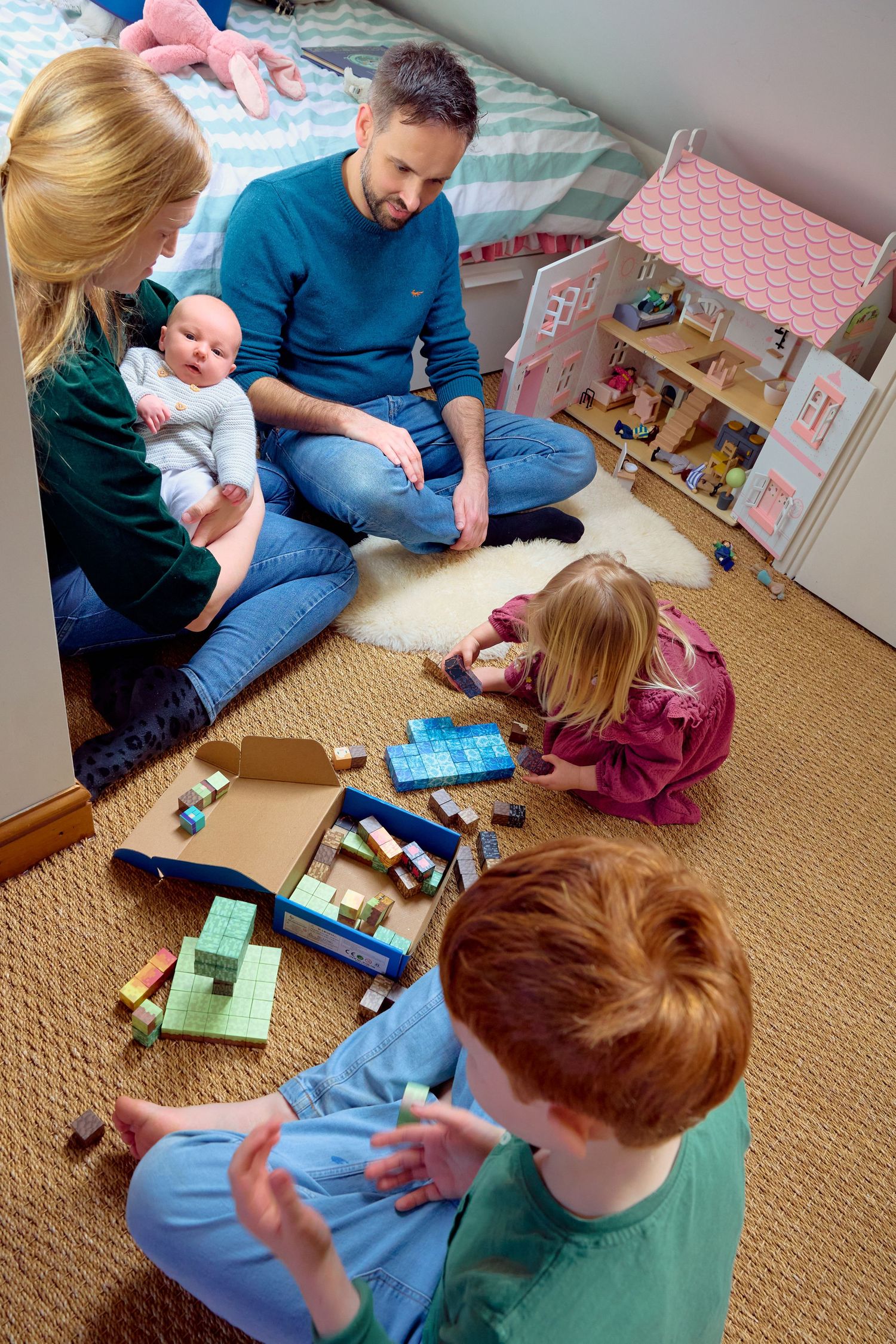 Family with baby and children playing with building blocks together on floor in cozy kids bedroom.