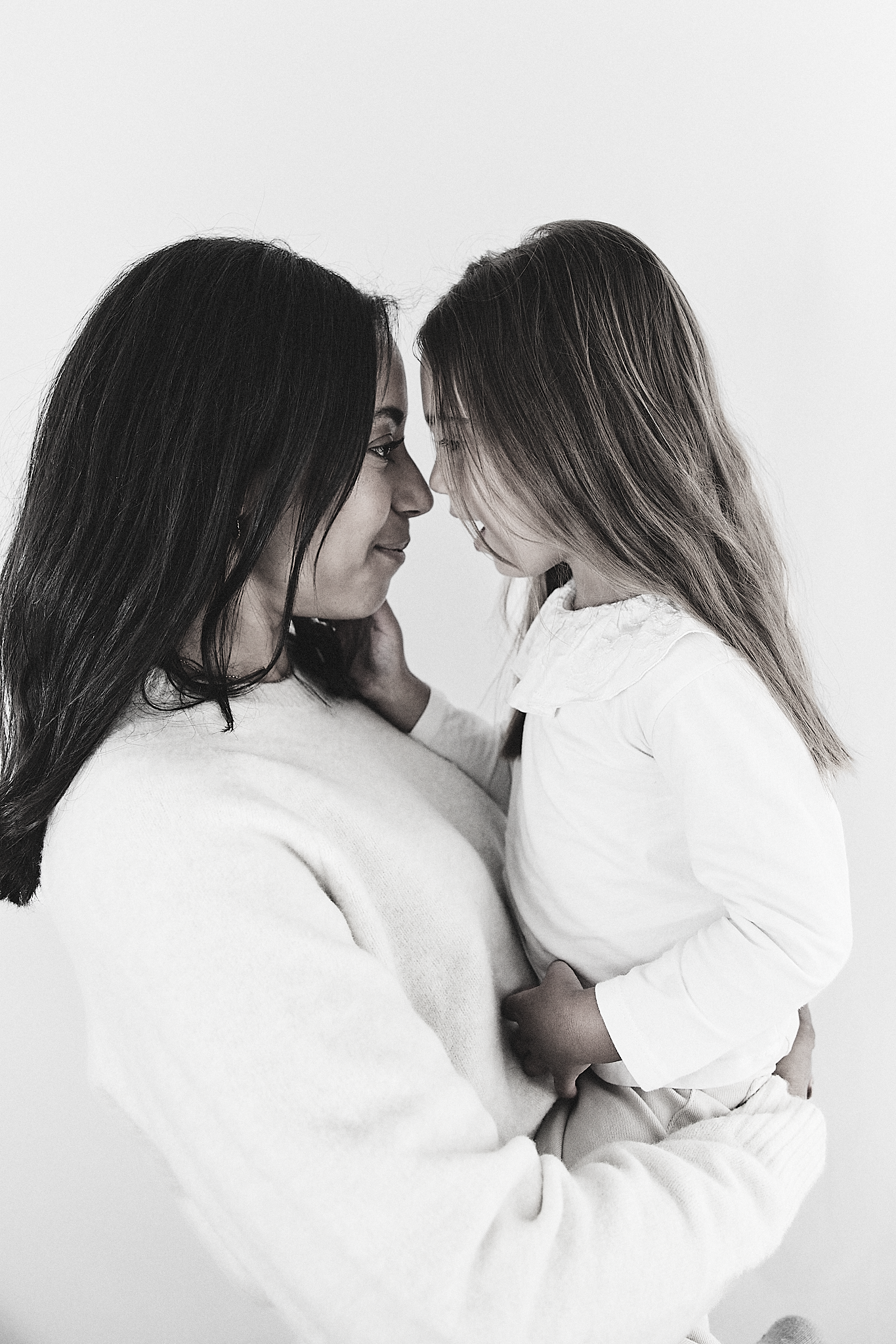 Black and white photo of a mother holding her young daughter close, both smiling with foreheads touching tenderly.
