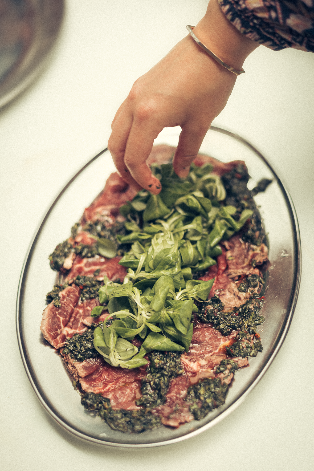Hand placing fresh greens on oval platter with pink and dark ingredients.