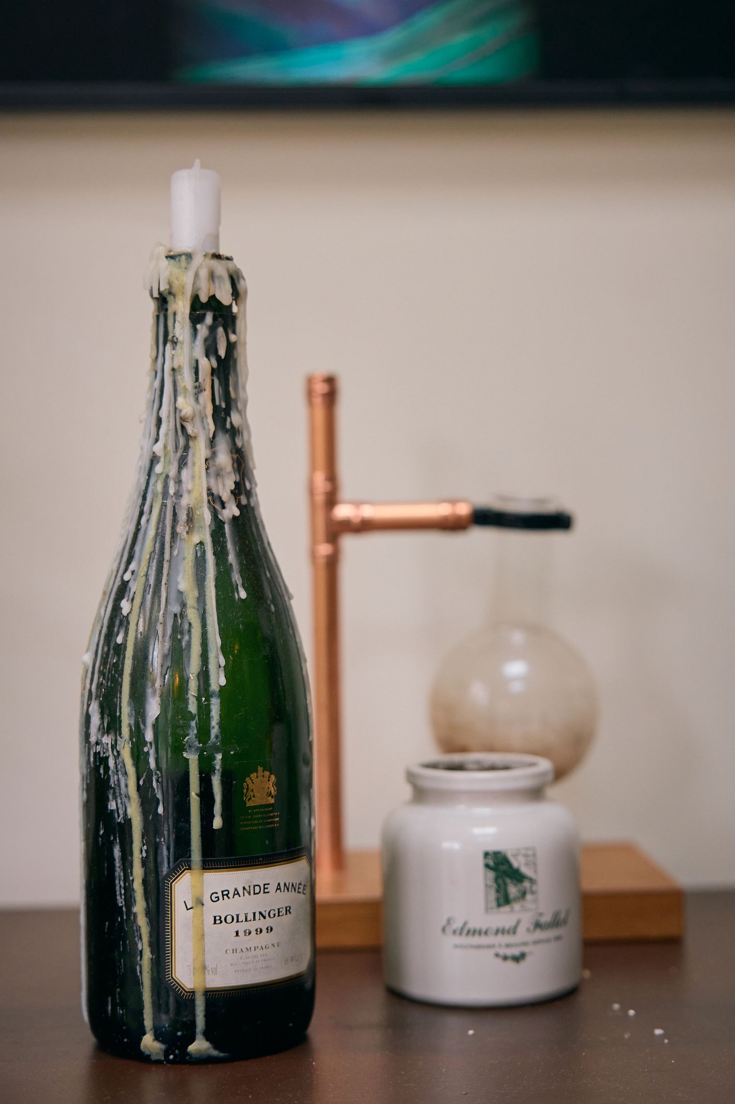 Bollinger La Grande Année champagne bottle used as a candle holder with white wax drips on a wooden surface.