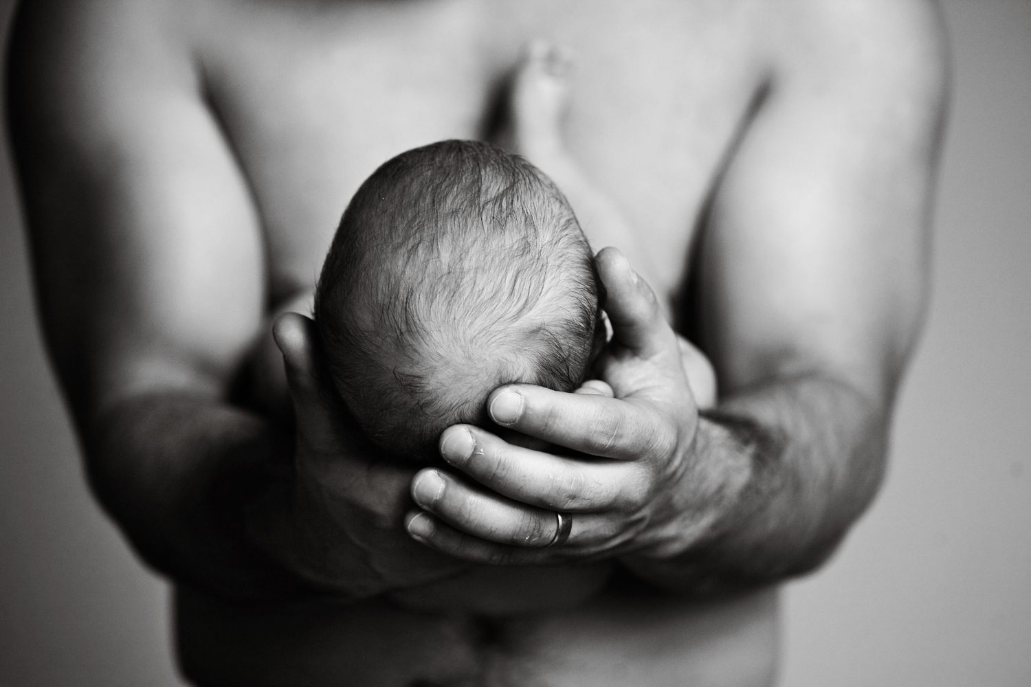 A dramatic black and white image of hands cradling a newborn.