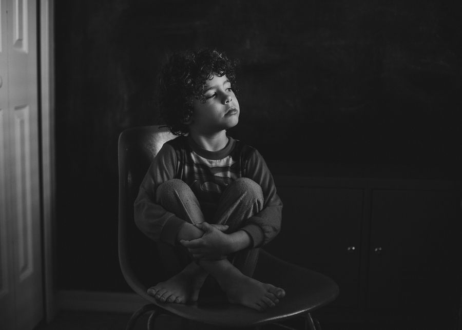 Moody black and white portrait of a person with curly hair sitting in contemplation.