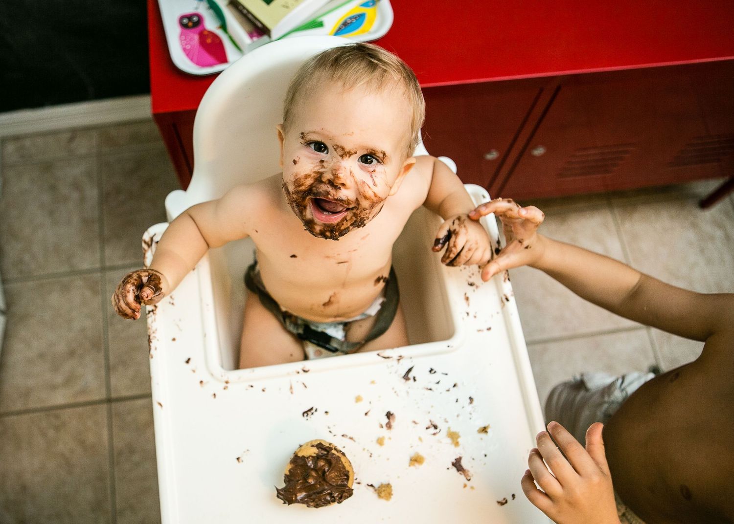 Messy mealtime scene with chocolate-covered baby in high chair.