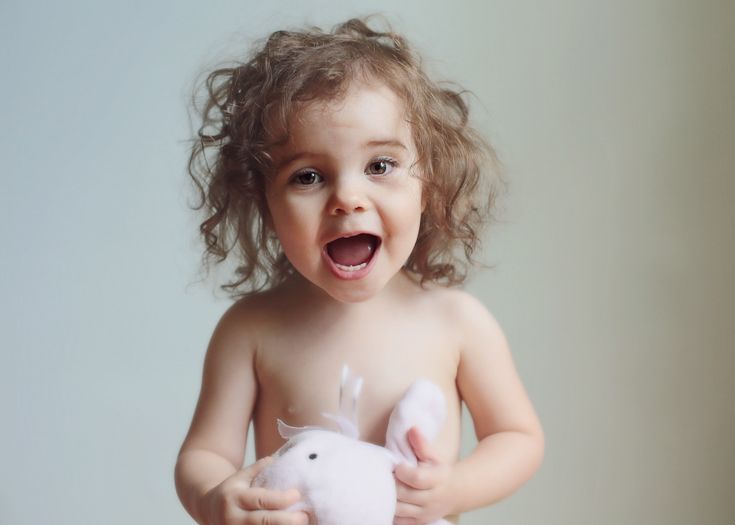 Happy toddler with curly hair holding a stuffed toy and laughing joyfully.