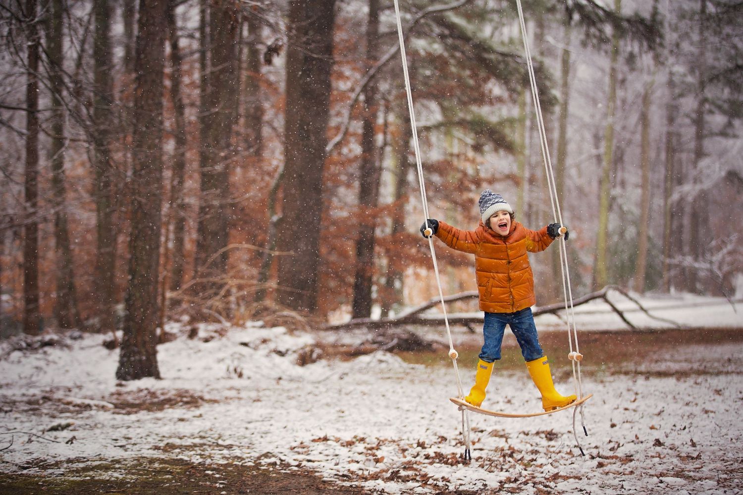 Figure in orange coat jumping with joy in snowy winter forest.