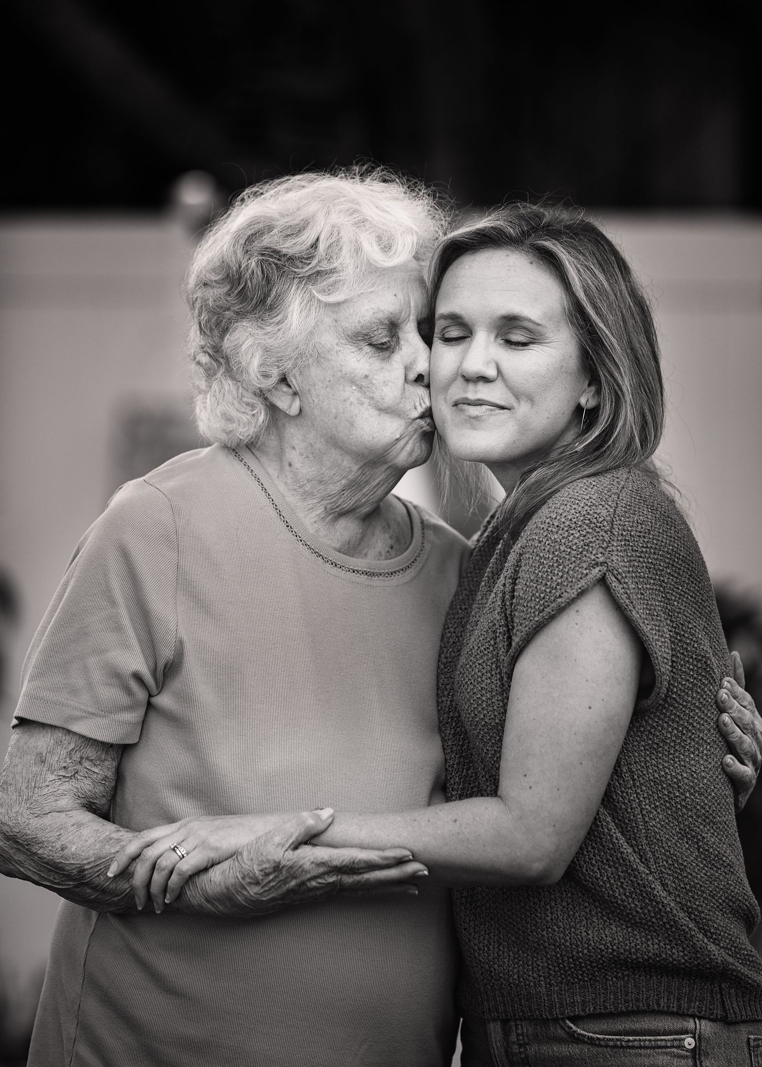 An intimate black and white portrait showing a tender moment between two women.