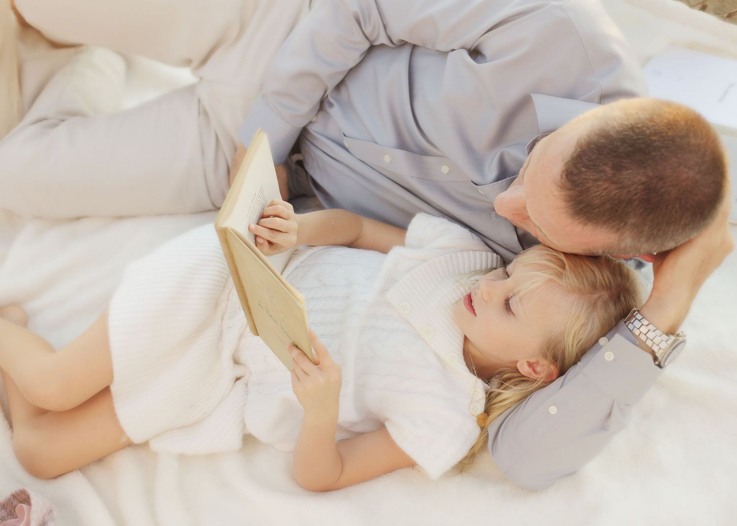 Parent and child share a tender moment lying together on white bedding.