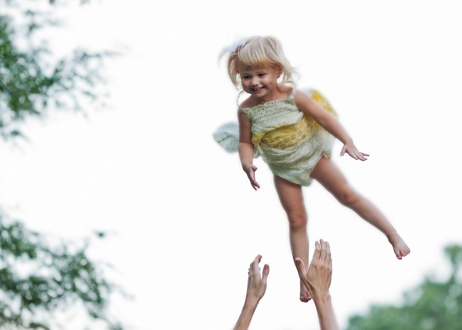 Joyful child being tossed in air wearing fairy wings outdoors.
