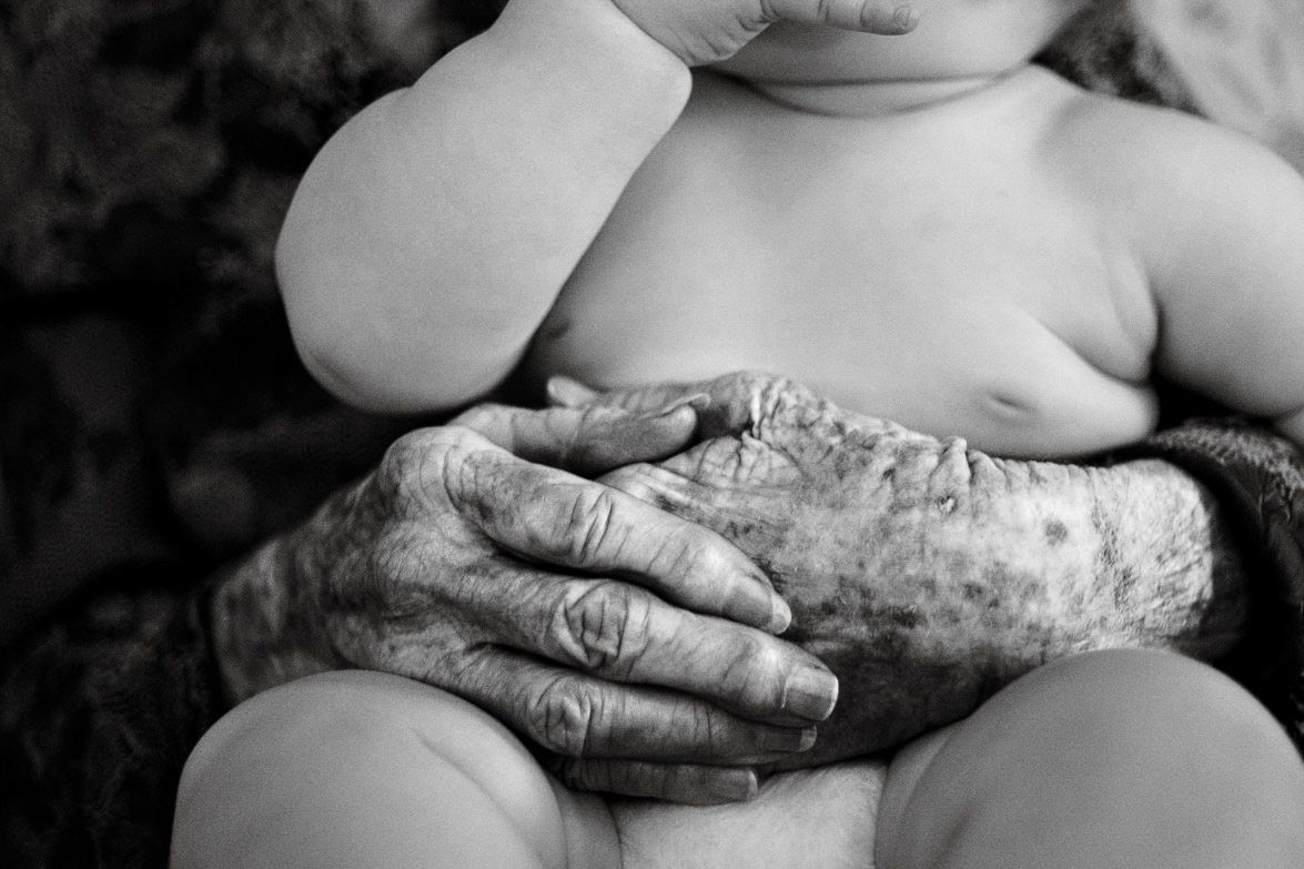 Close-up black and white image of elderly hands holding baby.