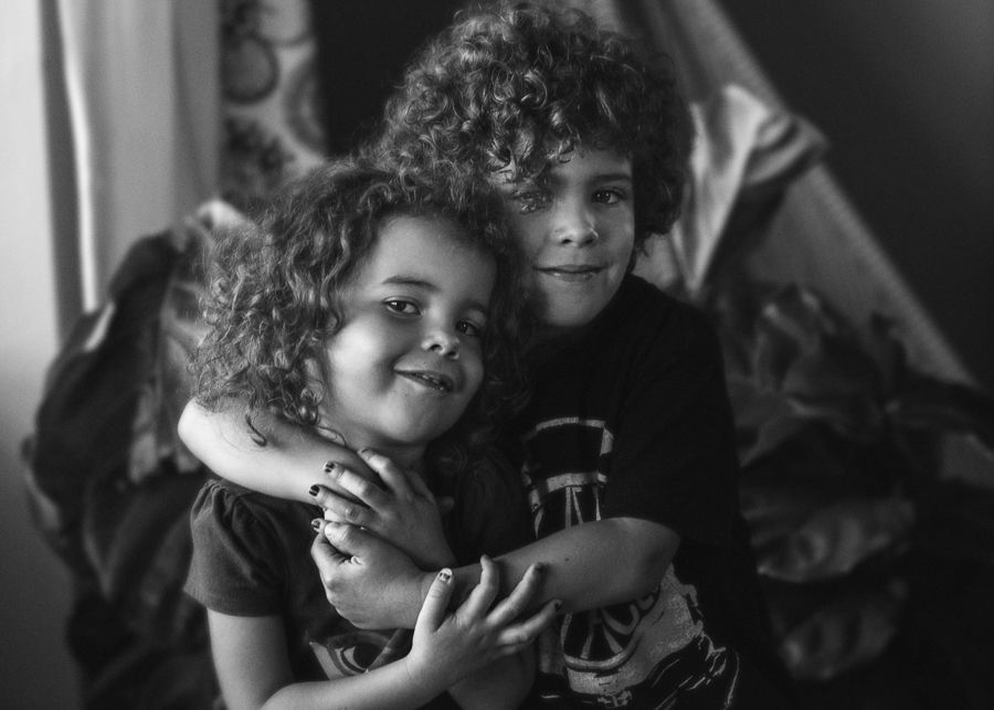 Black and white portrait of two young people with curly hair embracing and smiling together.