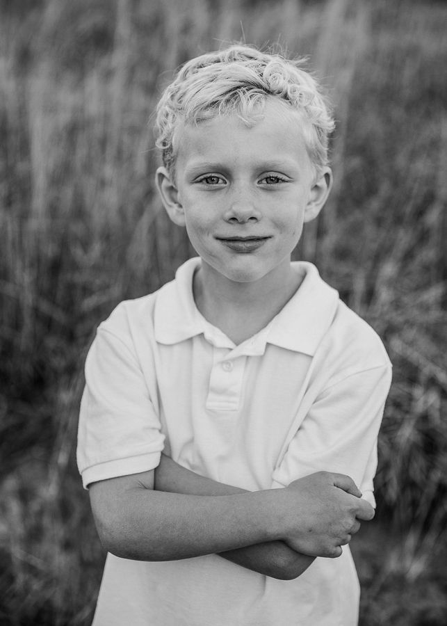 Black and white portrait of a young child in a white polo shirt with crossed arms.