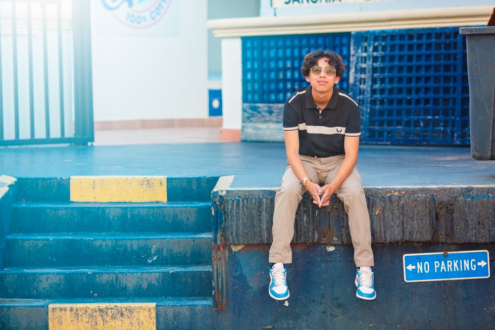 Young man sitting on steps near a No Parking sign in front of a blue building outdoors.