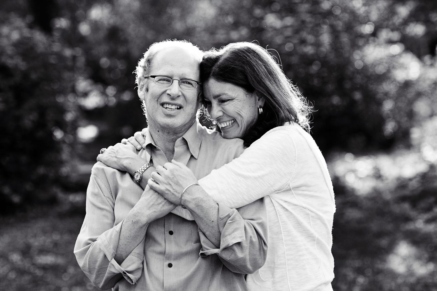 A couple shares a candid moment of laughter while embracing outdoors in black and white.