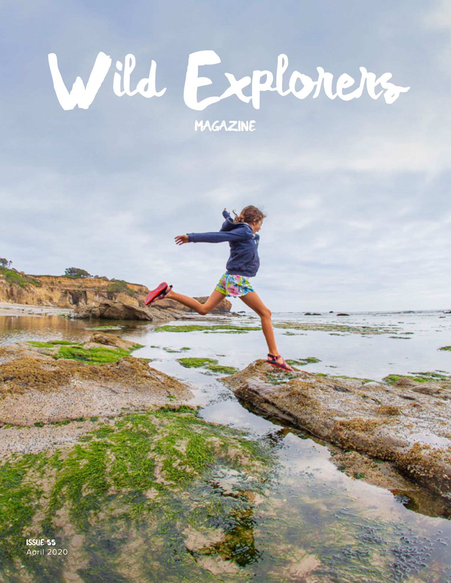 Person leaping across rocky tide pools on a misty coastal beach for Wild Explorers magazine cover.