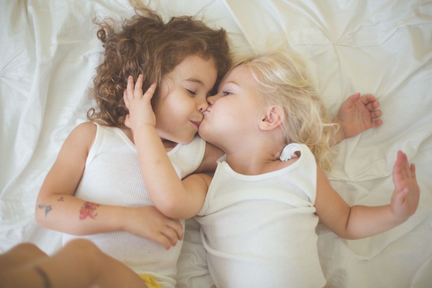 Two children sleeping peacefully on white bedding.