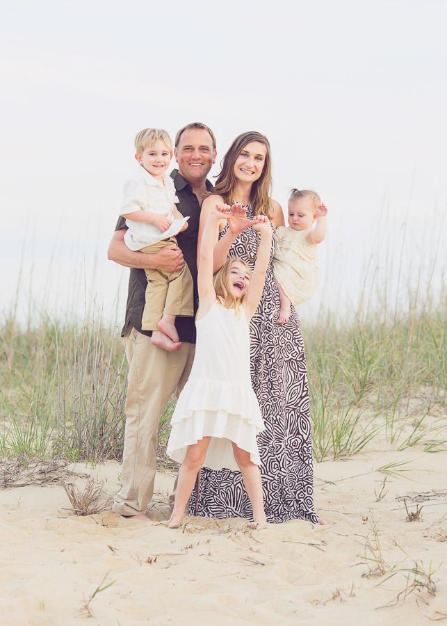 Family of four posing together on sandy dunes against a bright sky background.