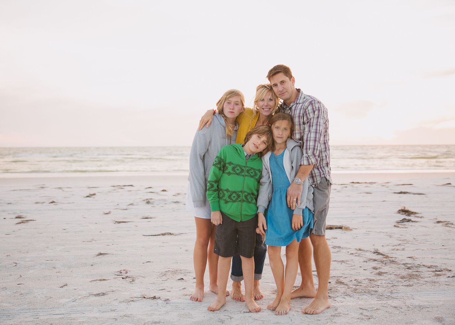 Family of five poses together on beach at sunset.