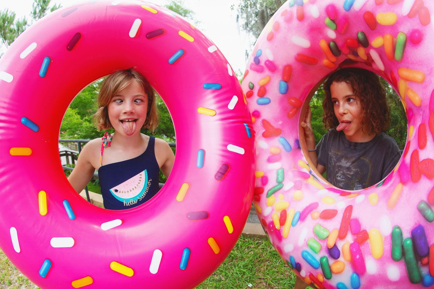 Two people peek through colorful donut-shaped pool floats with sprinkle patterns.