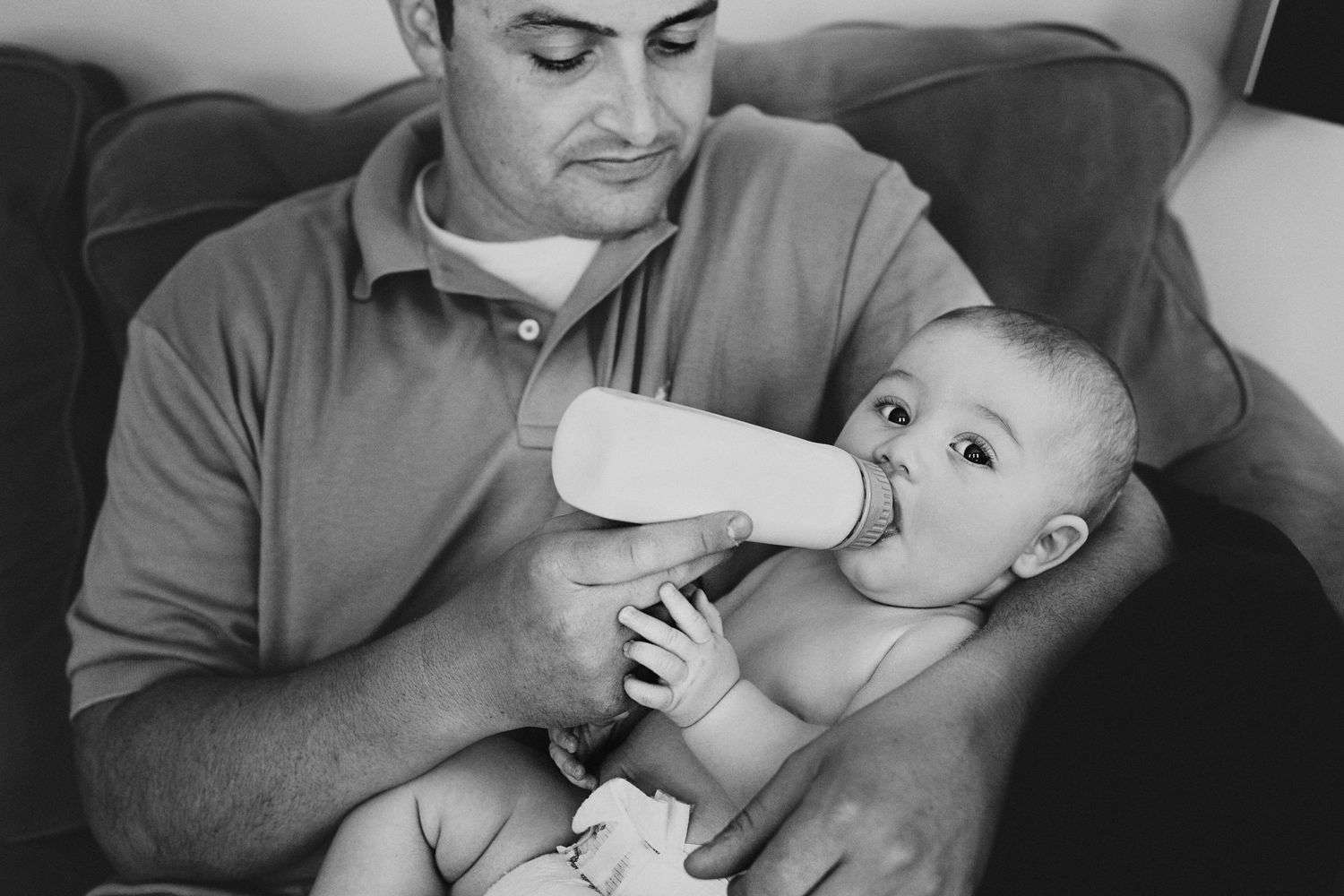 A tender moment of bottle feeding on a couch captured in black and white.