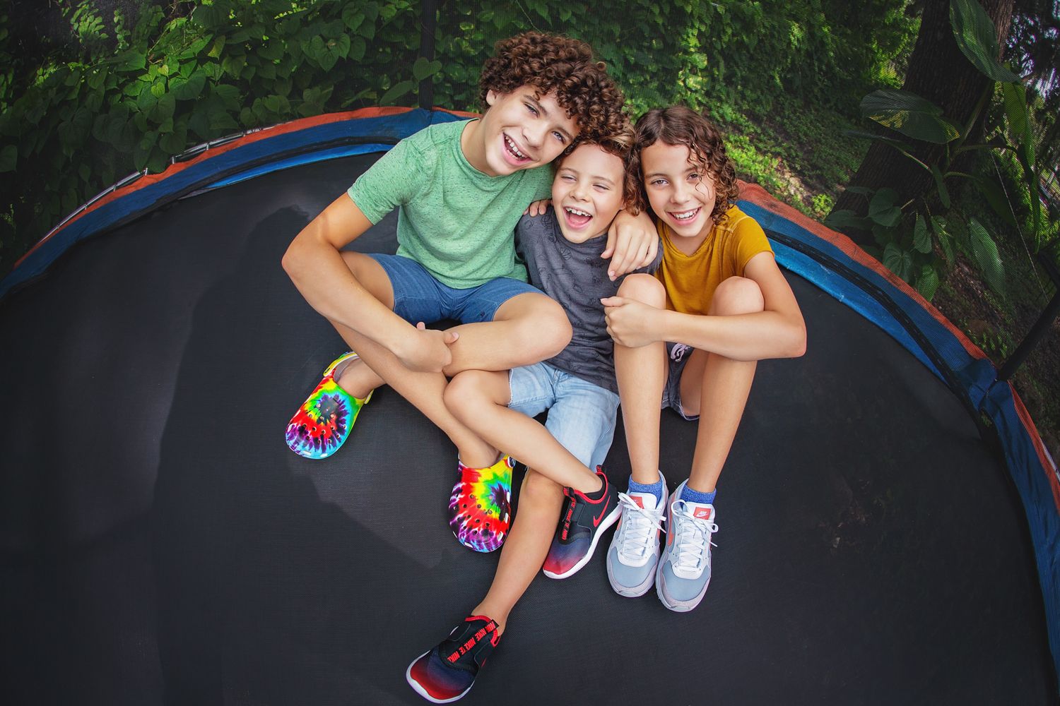 Three friends sitting together and smiling on backyard trampoline.