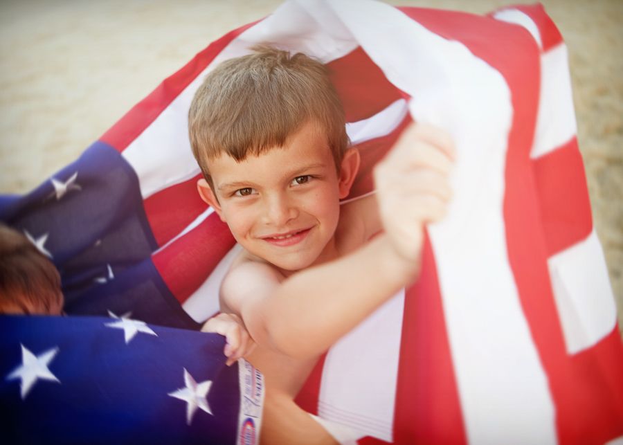 Young child wrapped in American flag smiling at camera with patriotic spirit.