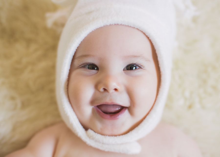 Close-up portrait of a smiling baby wearing a white hooded garment.