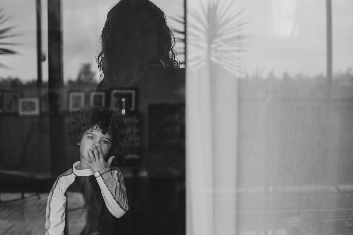 A reflective silhouette photograph through window glass with palm trees in background.