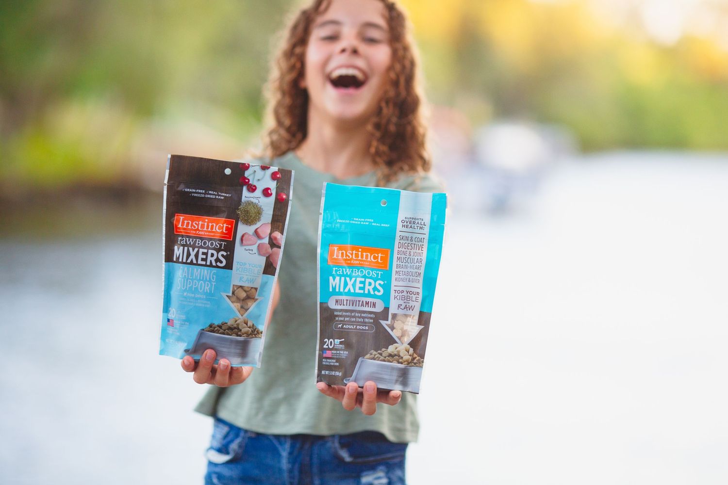 Someone holding up two packages of Instinct brand pet food products outdoors.