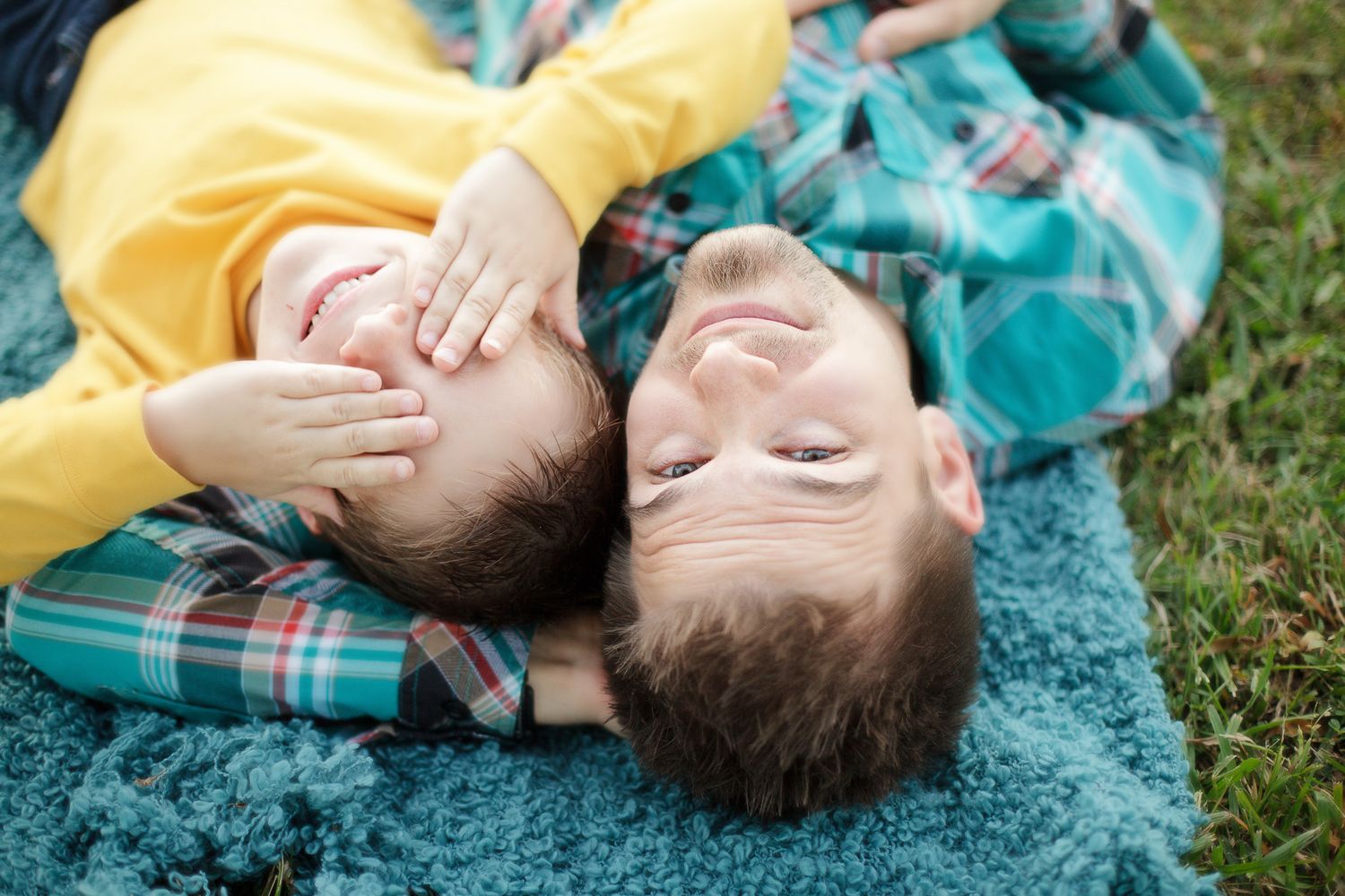 Two children lying on a plaid blanket outdoors sharing laughter together.