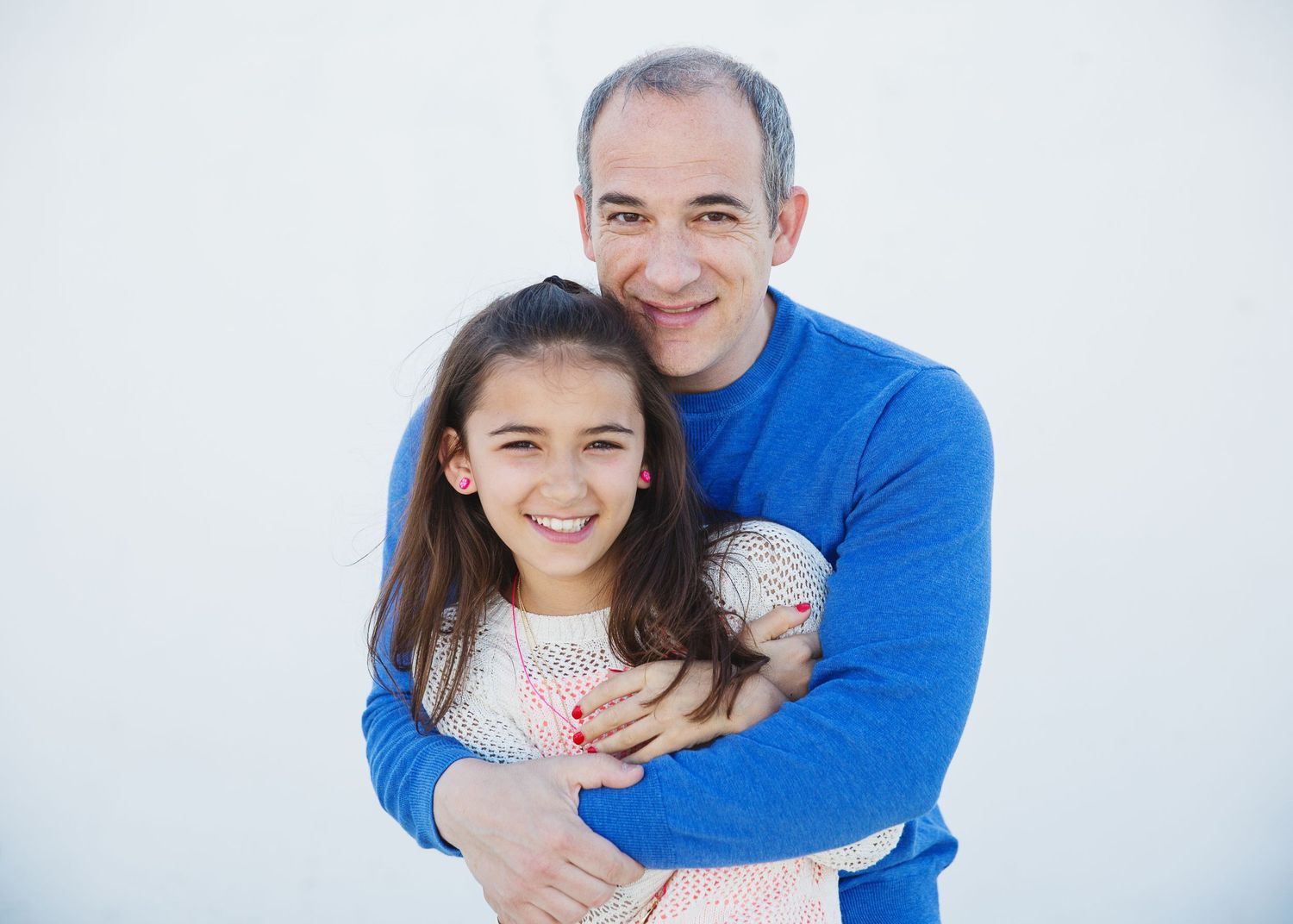 Portrait of a father and daughter embracing against a white background.